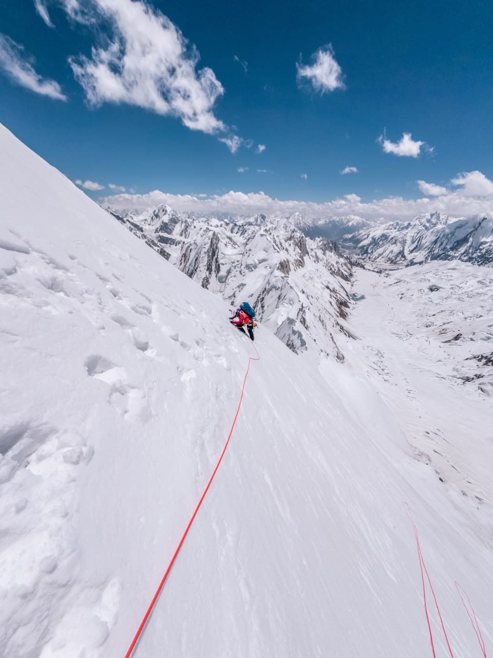 Climber ascending steep snow on Spantik with a rope trailing below